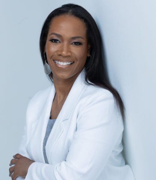 Portrait of Candice Ramsey looking directly at the camera and smiling. She has long, dark hair and her arms are folded. She is wearing a white jacket and is standing against a white backdrop.