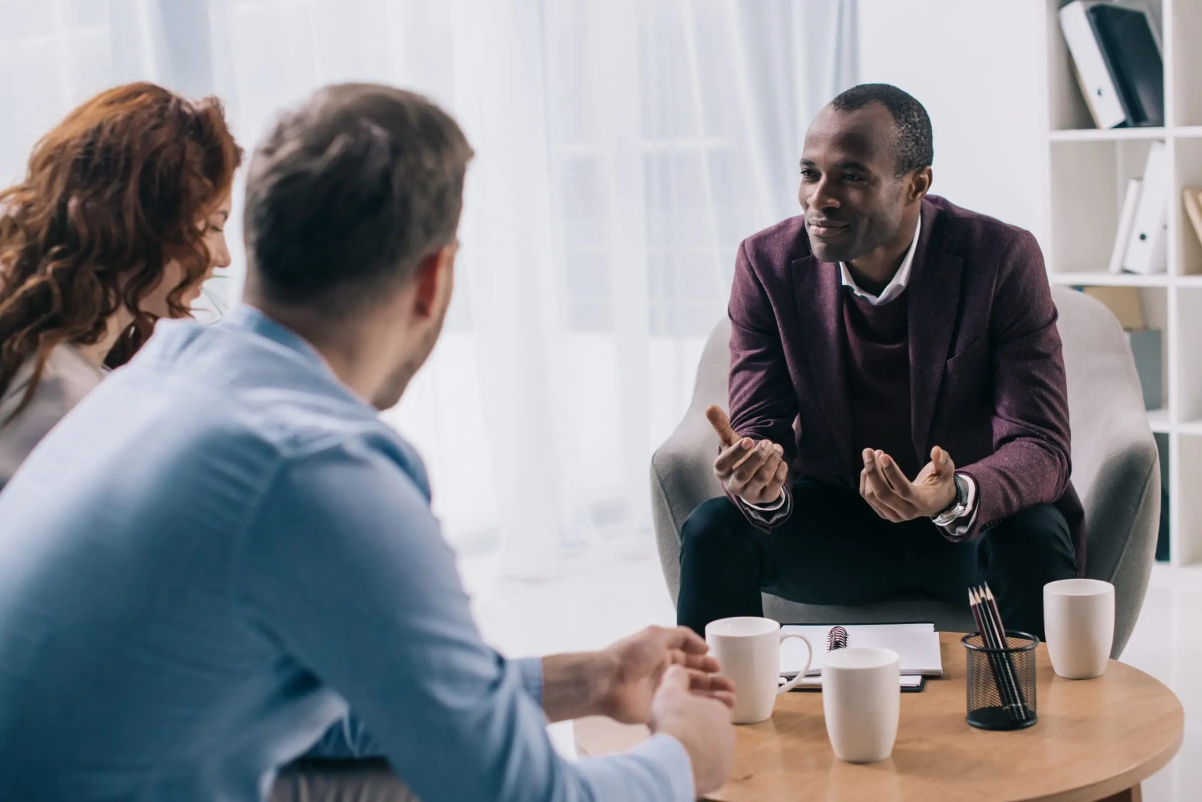 Smiling african american counselor talking to young couple in of
