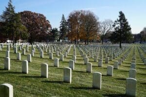 Image of Philadelphia National Cemetery with rows of white grave stones on green grass. Trees edge along the border of the image. 