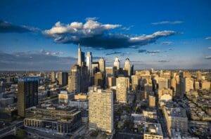 Picture of the skyline of Philadelphia at dusk with clouds in the dark blue sky and sunlight casting long shadows. 