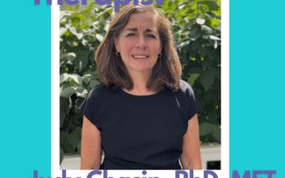 A professional photo of Judy Chasin, PhD, MFT, featured as a Paoli-based staff therapist at Council for Relationships. She is wearing a black top and standing outdoors in front of green foliage. Text on the image reads: "Featured Paoli Therapist – Judy Chasin, PhD, MFT – Staff Therapist, Paoli, PA & Online." Judy offers professional help to individuals and couples navigating burnout, grief, and symptoms of depression. She supports clients asking themselves questions like "how do you know you need therapy?" and "how to know if someone is depressed?" Judy provides therapy for grief and specializes in helping clients access expert, compassionate care.
