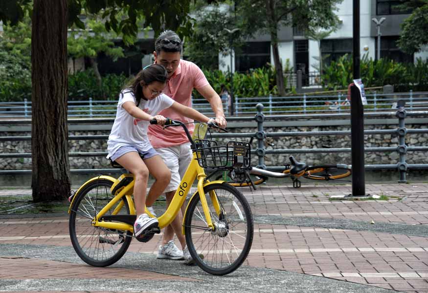 Father teaching daughter how to ride a bike in springtime in front of a canal
