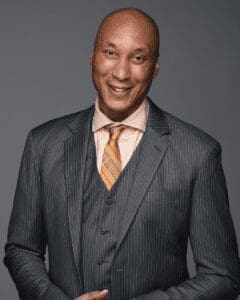 Picture of James Wadley wearing a grey suit with a light shirt and peach-colored tie. He is looking directly at the camera and is smiling. 
